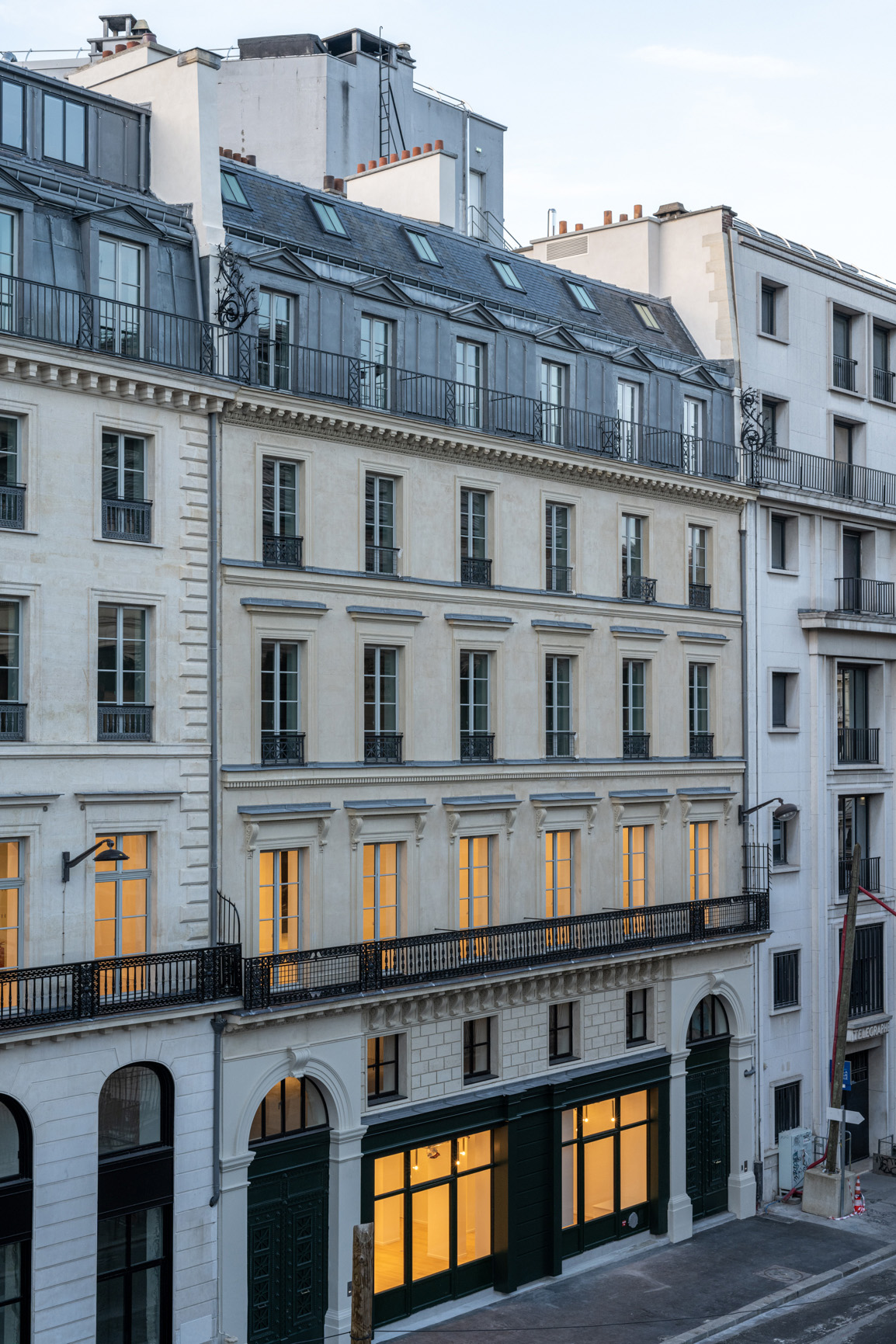 Façade en pierre d'un immeuble de bureaux parisien illuminé au rez-de-chaussée et premier étage.