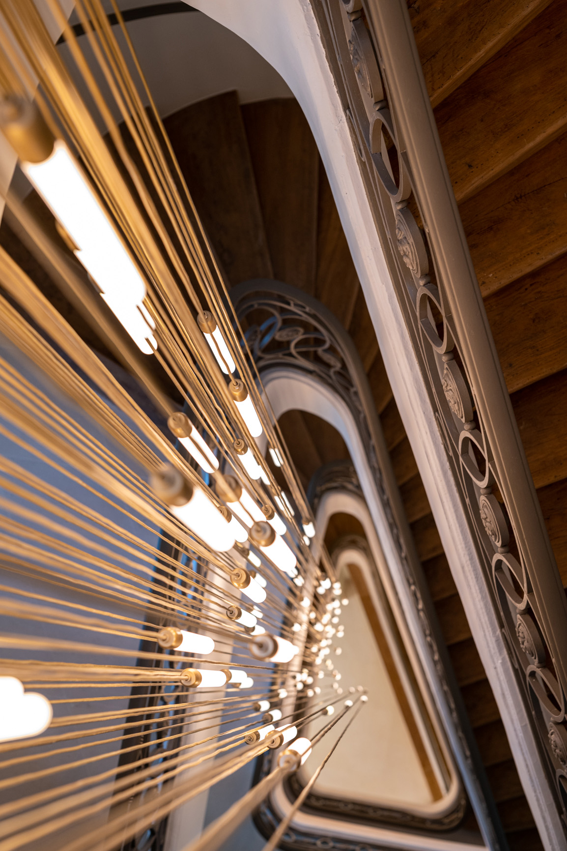 Luminaires dorés au centre d'un escalier monumental en bois et ferronneries dans un immeuble de bureaux sur la place de la Bourse.