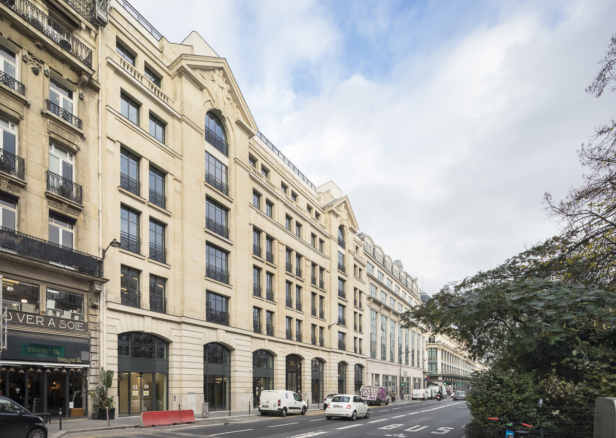 Façade en pierre parisienne d'un immeuble de bureaux avec un ciel bleu.