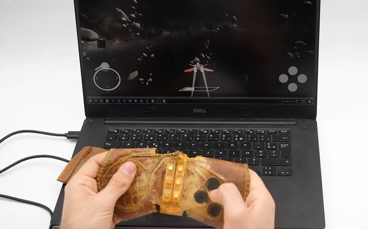 Une personne tient une manette de jeu video faite en kombucha, face à un écran d'ordinateur